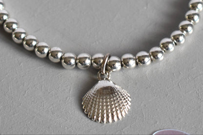 Close up of Sterling silver beaded bracelets with 4mm beads. Suspended from the bracelet  is a sterling silver clamshell. From the Ocean Collection of stacking bracelets.