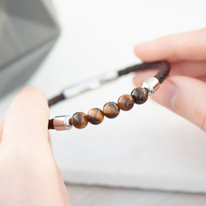 Detail of tiger's eye beads showing the natural colours within them. Brown woven leather bracelet with five tiger's eye beads. Barrel clasp engraved with initials and your own message