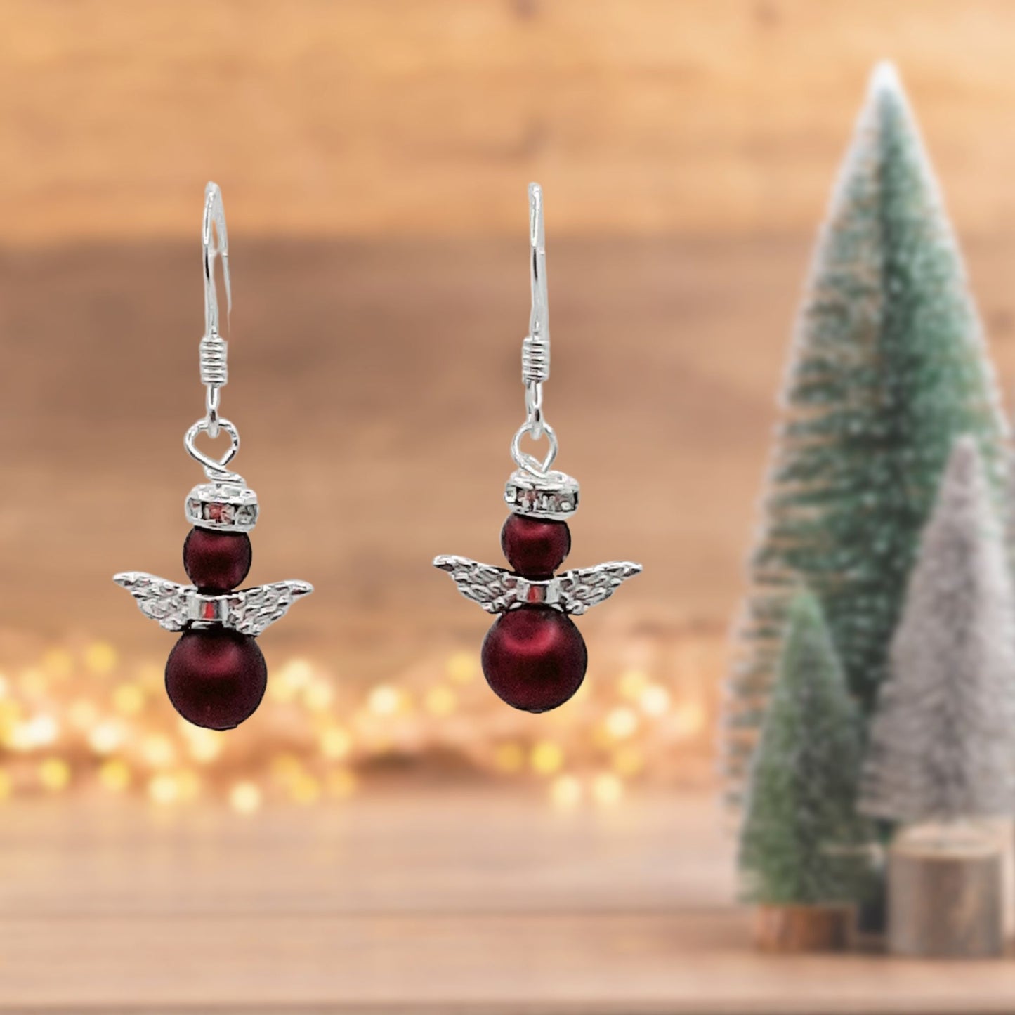 Pair of angel earrings made with burgundy pearls and incorporating angel wings and a crystal halo. Hung from sterling silver ear wires.