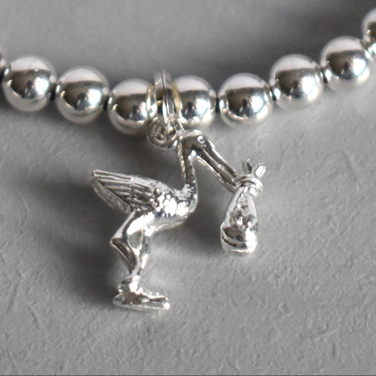 4mm sterling silver beads are threaded onto strong elastic from which is suspended a sterling silver stork carrying a little bundle. The perfect bracelet for new mums. Close up of charm