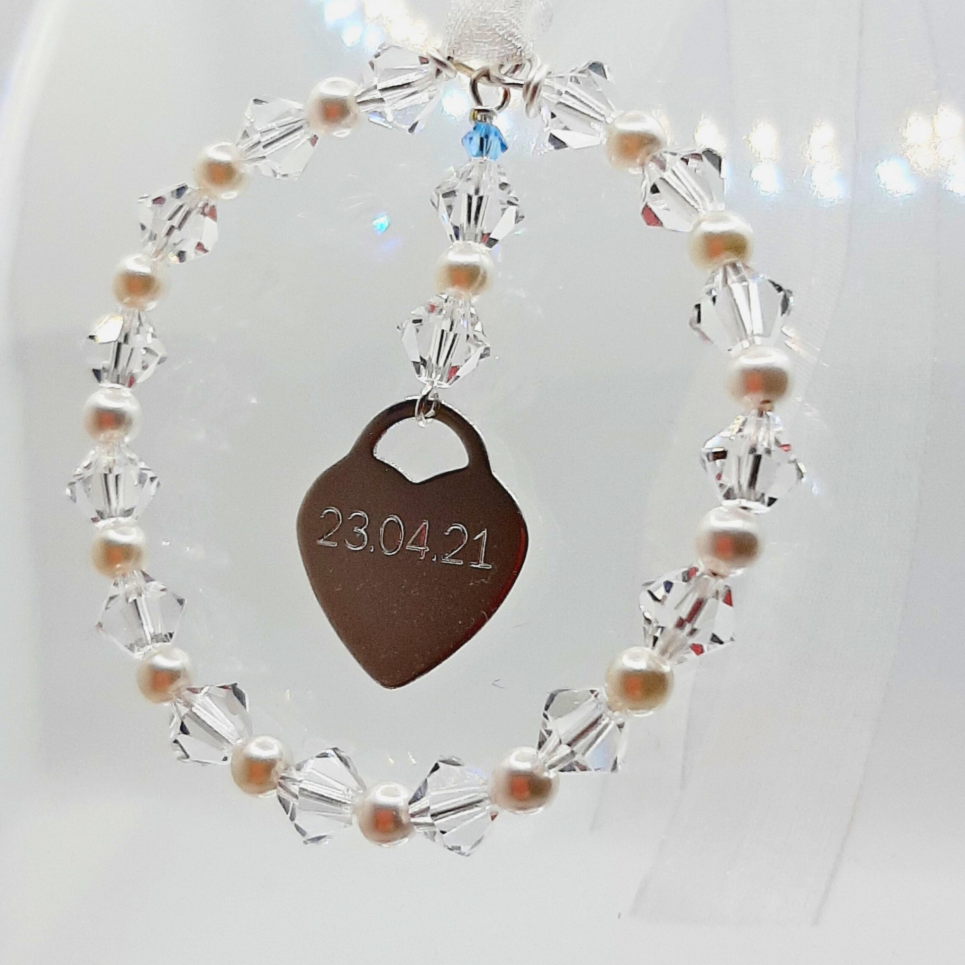 A wedding bouquet charm consisting of acircle of high quality crystals and glass pearls surround a sterling silver heart that can be engraved with names, dates or initials of your choice. Finished with white organza ribbon, the charm can be securely fastened to your wedding bouquet