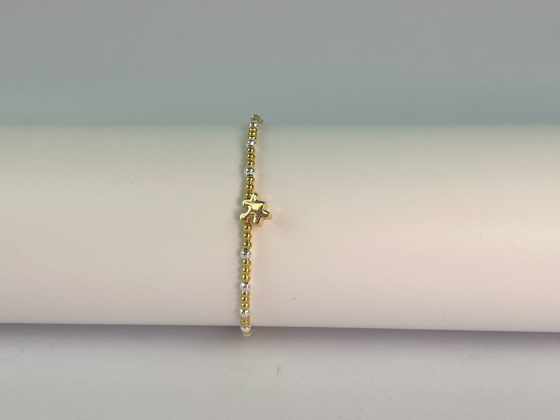 an elasticated gold and silver plated beaded bracelet with a jigsaw charm showing gold plated side