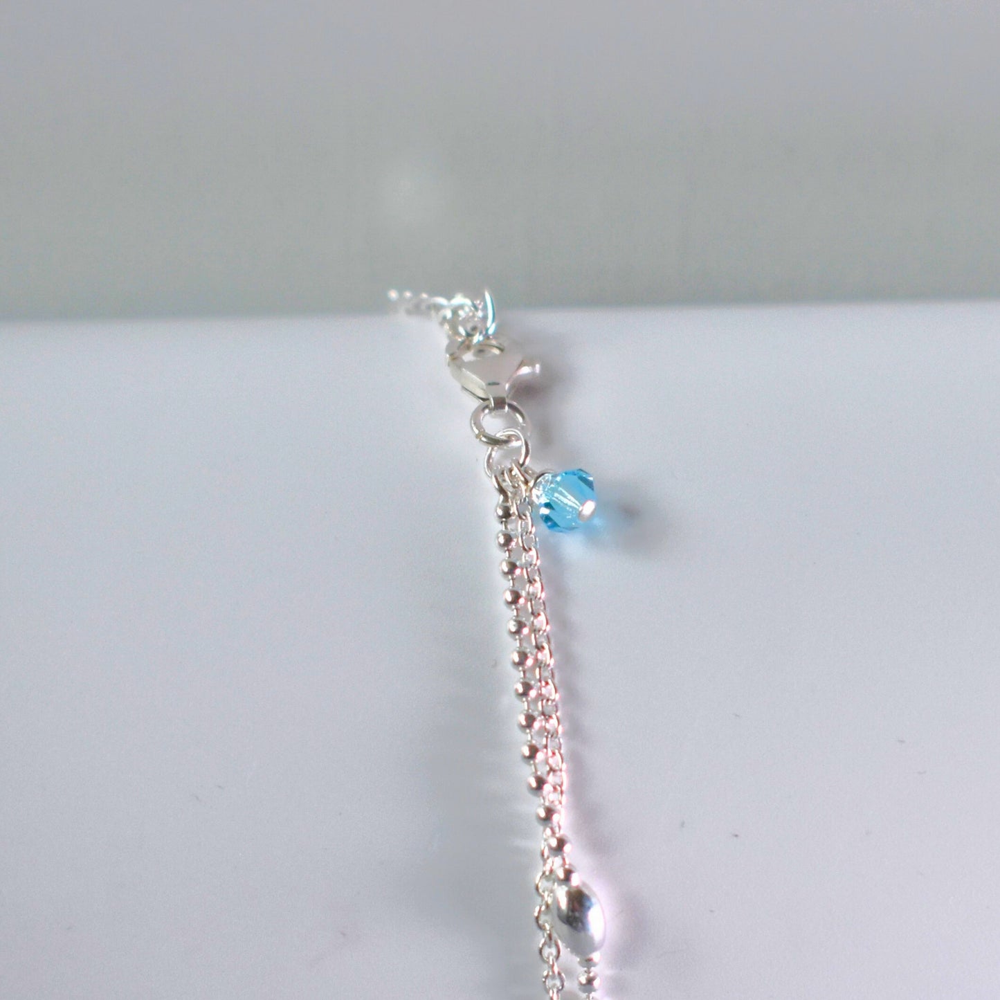 Close up of option blue crystal bead on sterling silver double strand beaded anklet with heart centre. 