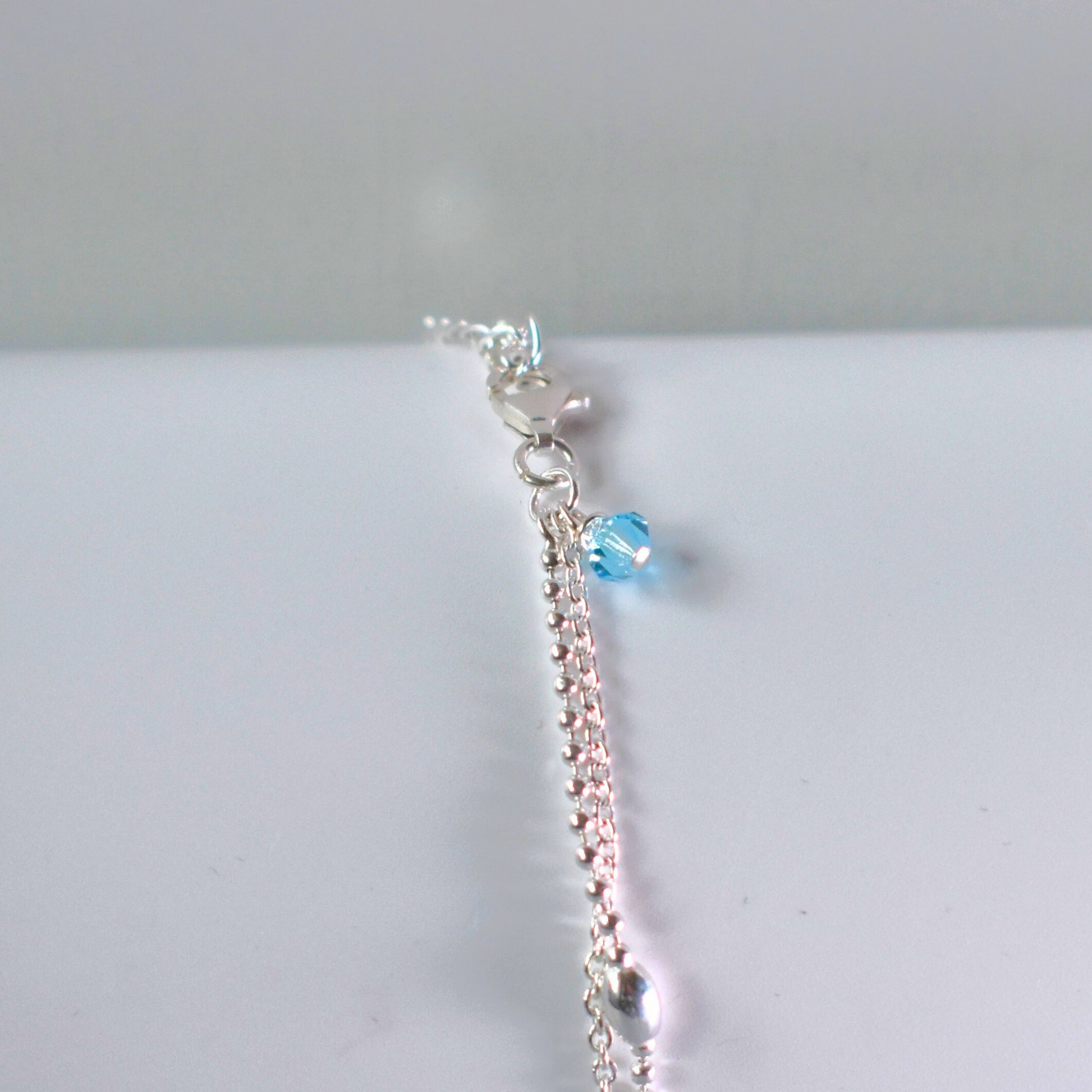 Close up of option blue crystal bead on sterling silver double strand beaded anklet with heart centre. 