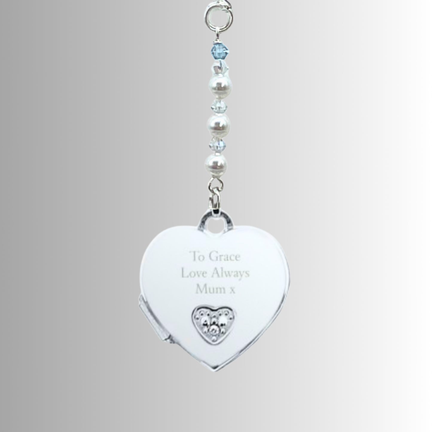 A sterling silver heart shaped locket wedding bouquet charm, engraved with wording of your choice on the front of the heart. The locket opens to add two photos of your choice. Suspended from a string of crystals and glass pearls with a tiny blue bead for your something blue.