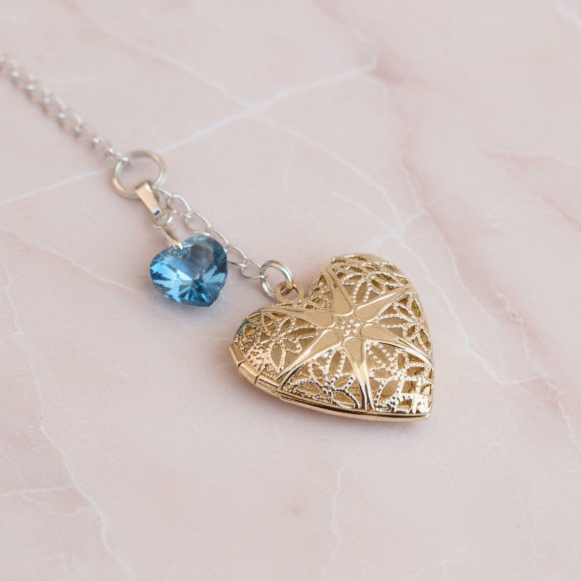Wedding bouquet locket. A filigree locket that opens to take one photo is suspended from a sterling silver chain and next to a high quality pale blue crystal heart. The chain ends in a lobster clasp so that the charm can be fastened securely to th Bride's bouquet