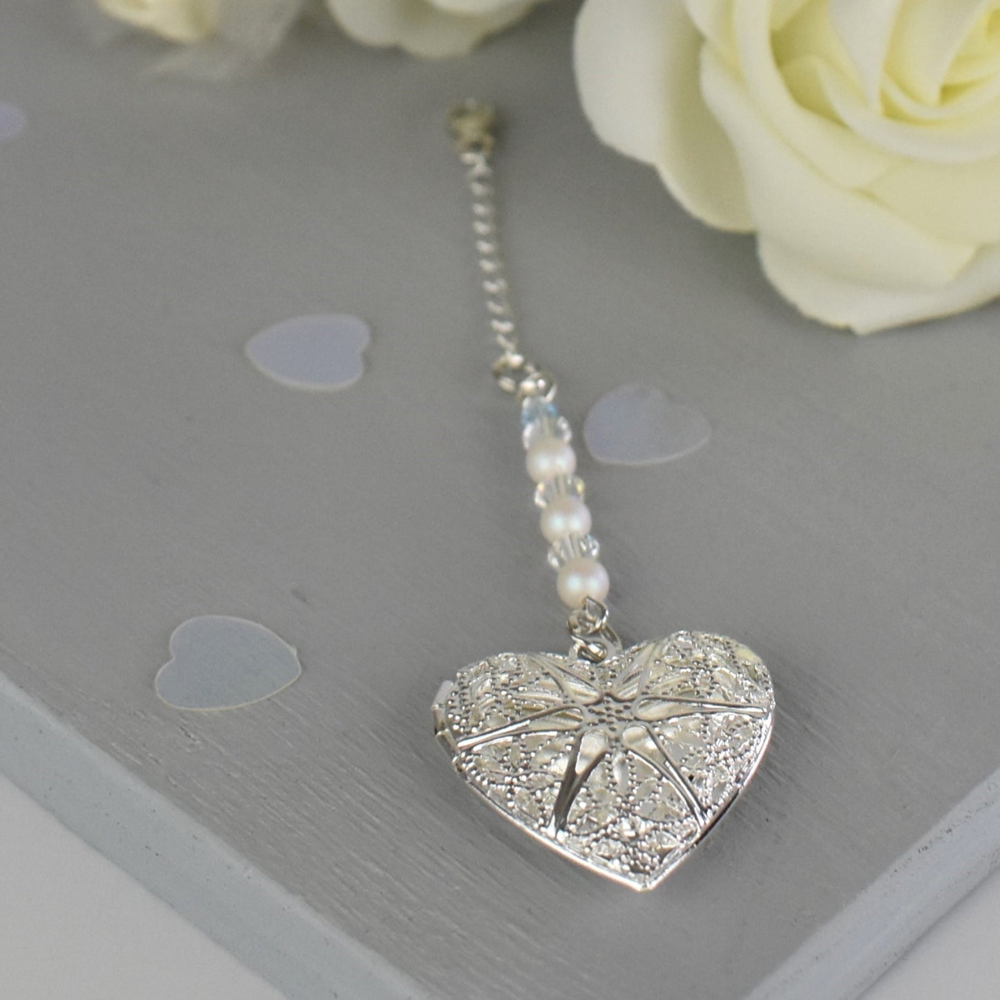 Heart shaped filigree locket opens to take one photo. Suspended from a line of glass pearls and Austrian crystals and finished with a tiny blue bead. The charm is suspended from a sterling silver chain and lobster clasp to fasten securely to a wedding bouquet.