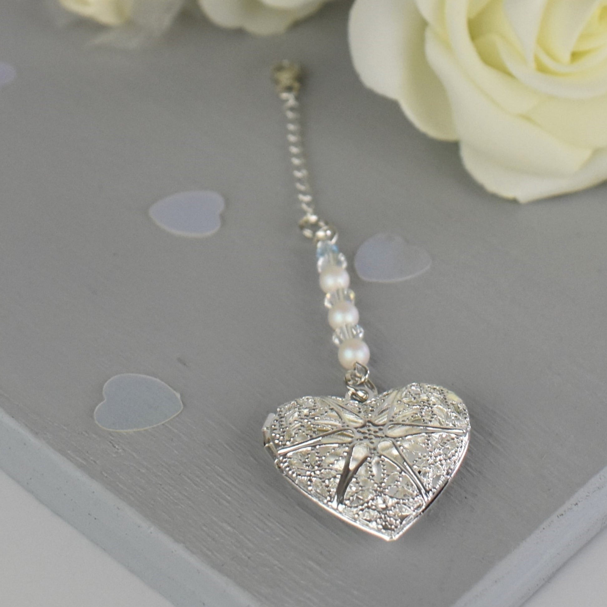 Heart shaped filigree locket opens to take one photo. Suspended from a line of glass pearls and Austrian crystals and finished with a tiny blue bead. The charm is suspended from a sterling silver chain and lobster clasp to fasten securely to a wedding bouquet.