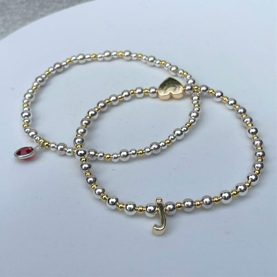 Bracelet with gold and silver plated beads on elastic and crystl birthstone and a gold and silver plated beaded initial bracelet with gold plated initial and heart.