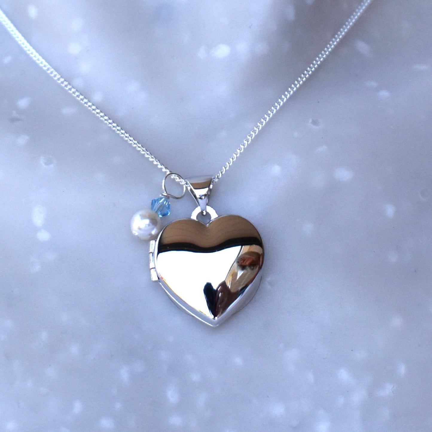 sterling silver heart locket, opens to allow for two photos to be fitted. Finished with a white glass pearl and tiny blue crystal.