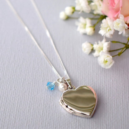 Sterling silver heart shaped locket on a sterling silver chain. Accompanied by a tiny white glass pearl and blue crystal