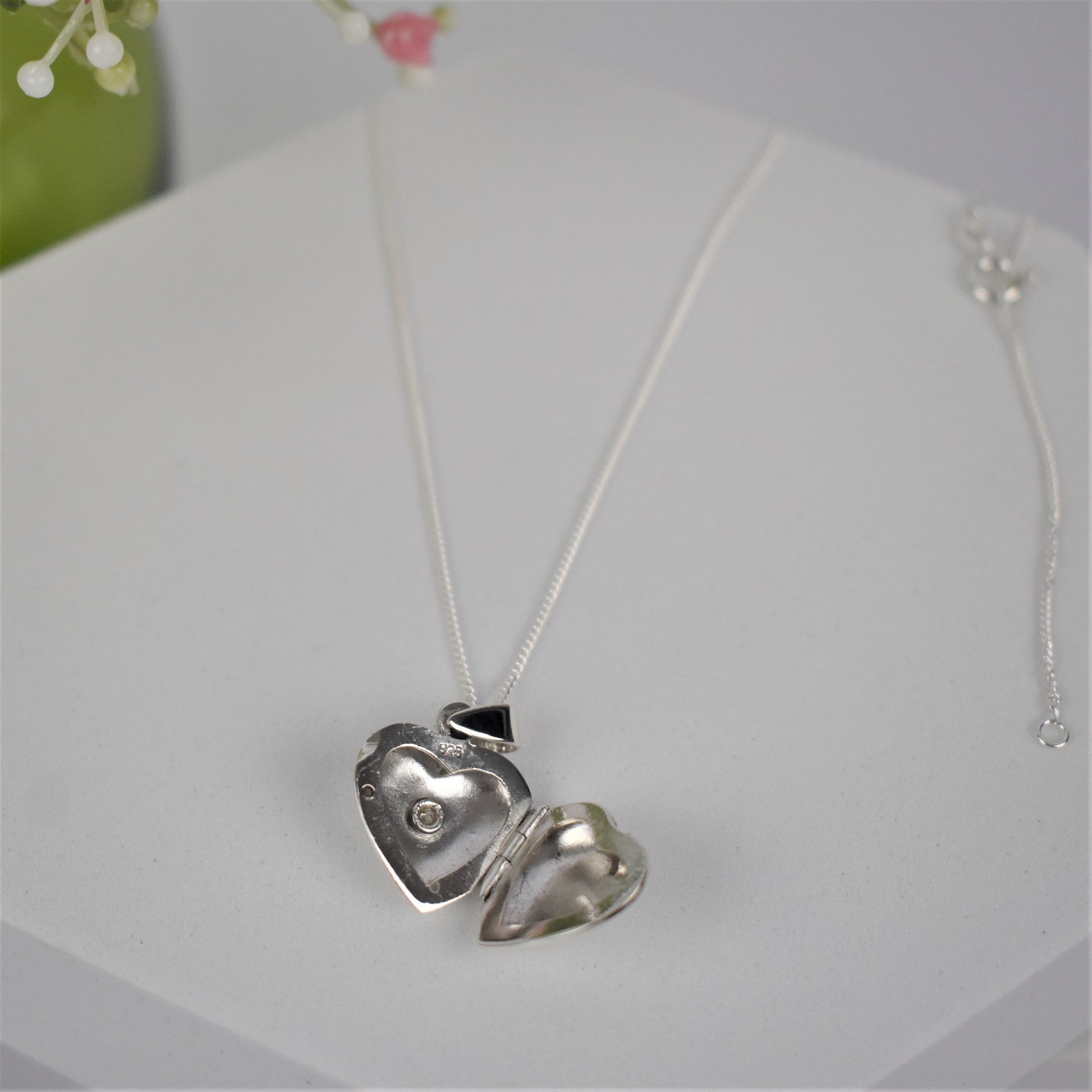 Silver heart-shaped opening locket necklace with a cubic zirconia stone in the centre shown with locket open