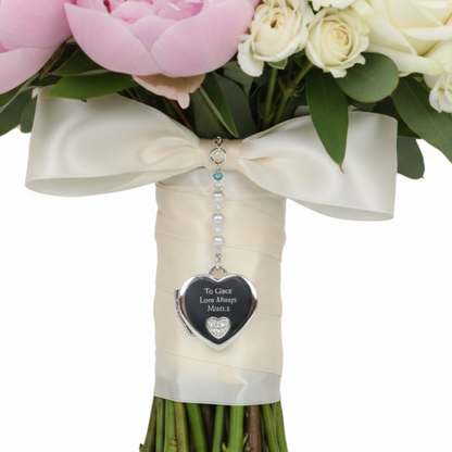Sterling silver heart shaped locket wedding bouquet charm. Shown on wedding bouquet. Suspended from a string of crystals and glass pearls with a tiny something blue bead