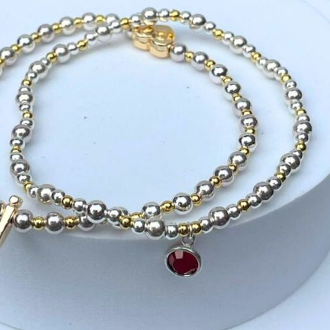 two colour birthstone bracelet. Elasticated bracelets of gold and silver plated beads with a crystal birthstone. Shown with two colour initial bracelet.