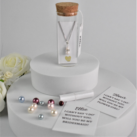 Double pearl drop pendant on silver chain is contained within a glass bottle with a scroll bridesmaid request. Bottle is finished with label  showing bridesmaid's name