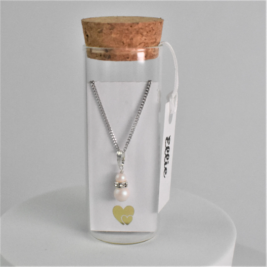Double pearl drop pendant on silver chain is contained within a glass bottle with a scroll bridesmaid request. Bottle is finished with label showing bridesmaid's name