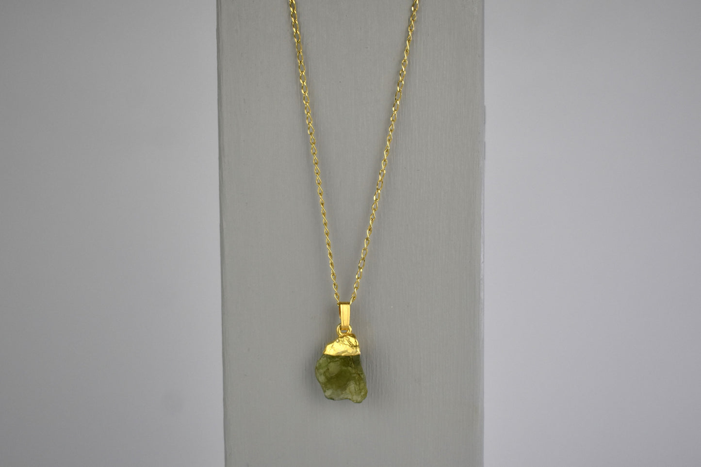 peridot raw crystal gem shown with sterling silver gold plated tip and suspended from a sterling silver gold plated chain. Peridot is the birthstone for August