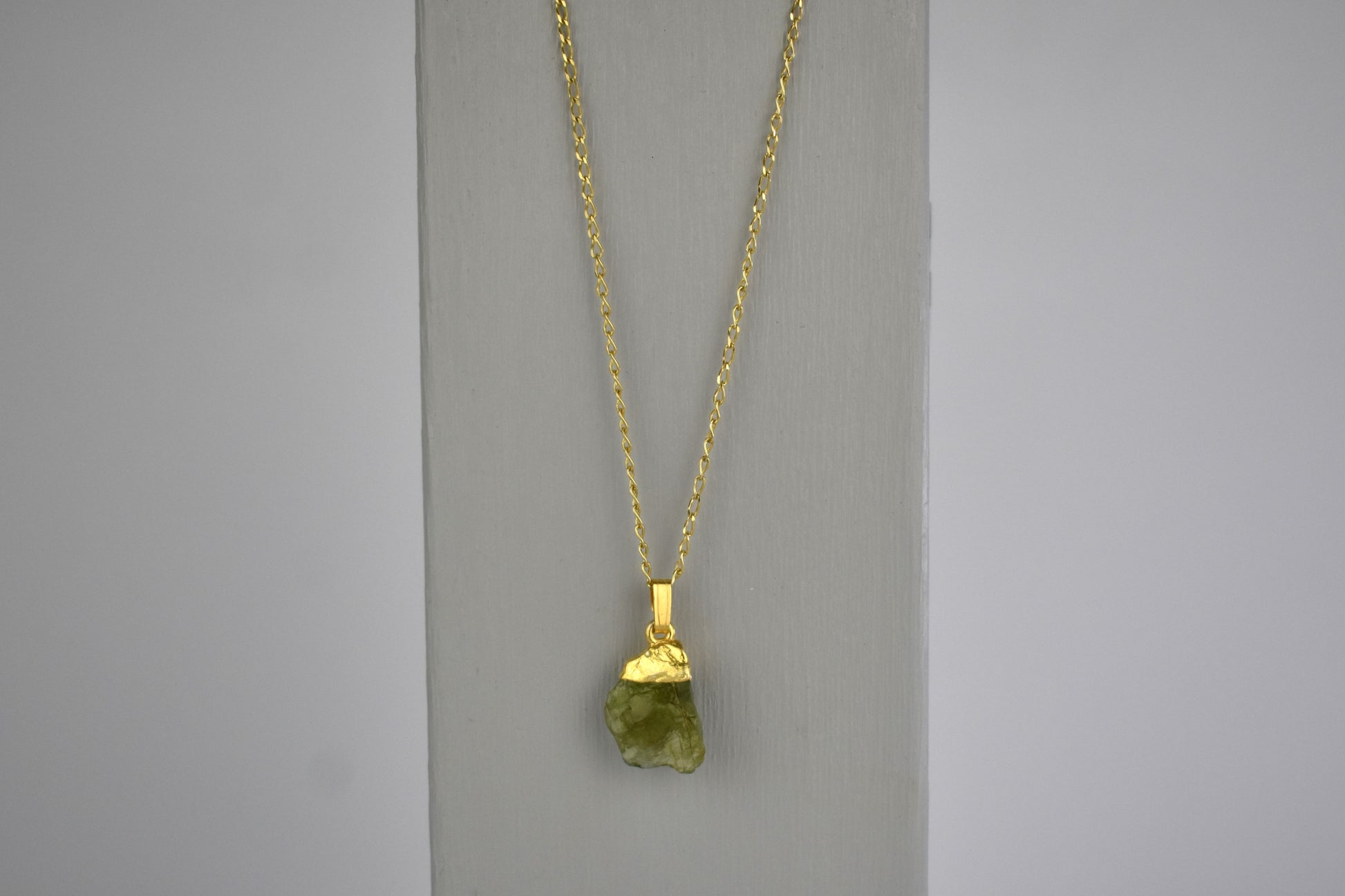 peridot raw crystal gem shown with sterling silver gold plated tip and suspended from a sterling silver gold plated chain. Peridot is the birthstone for August