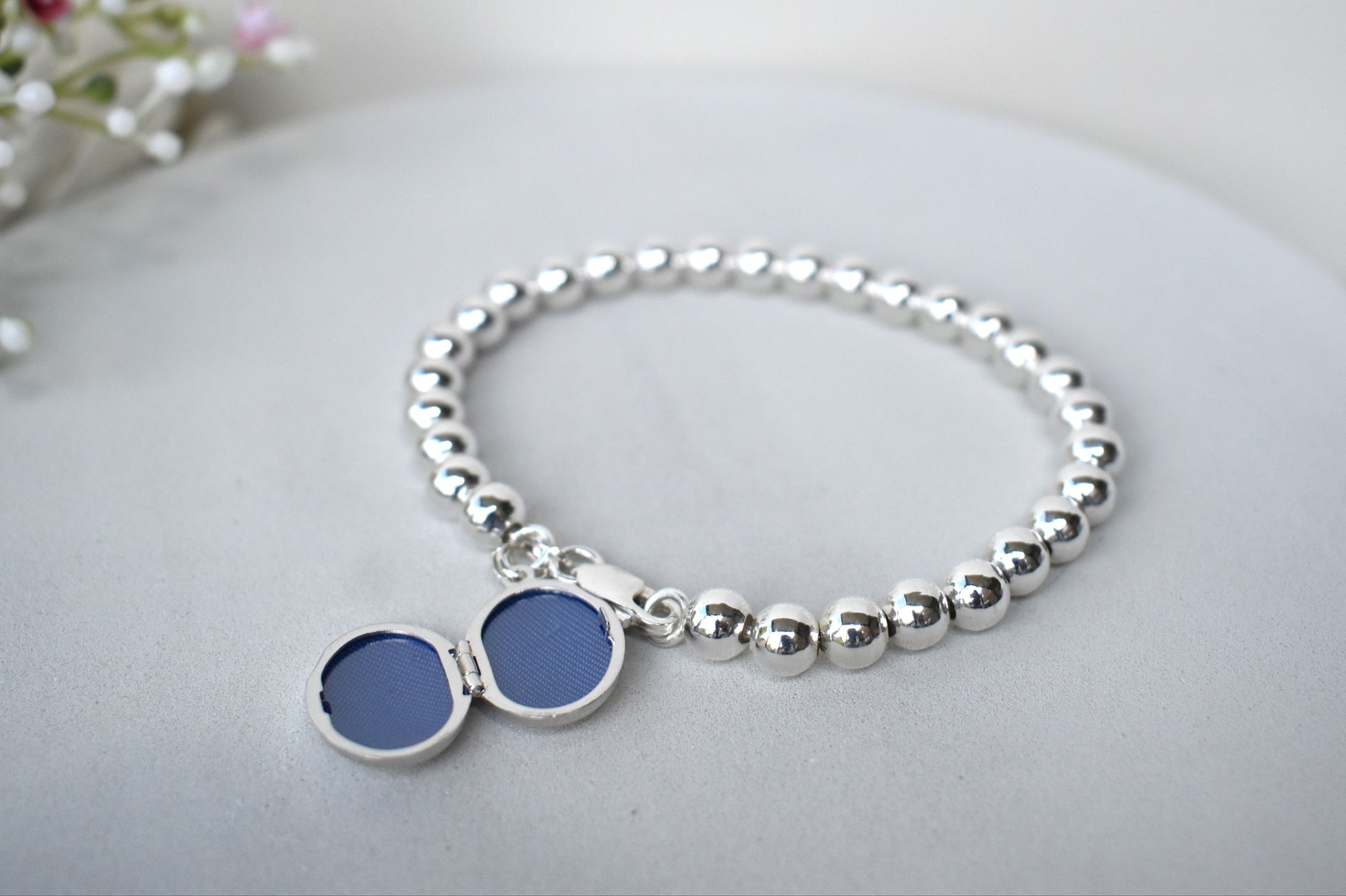 Sterling silver beaded bracelet with a lobster clasp. Next to the clasp is an oval locket that can be engraved with the wording of your choice