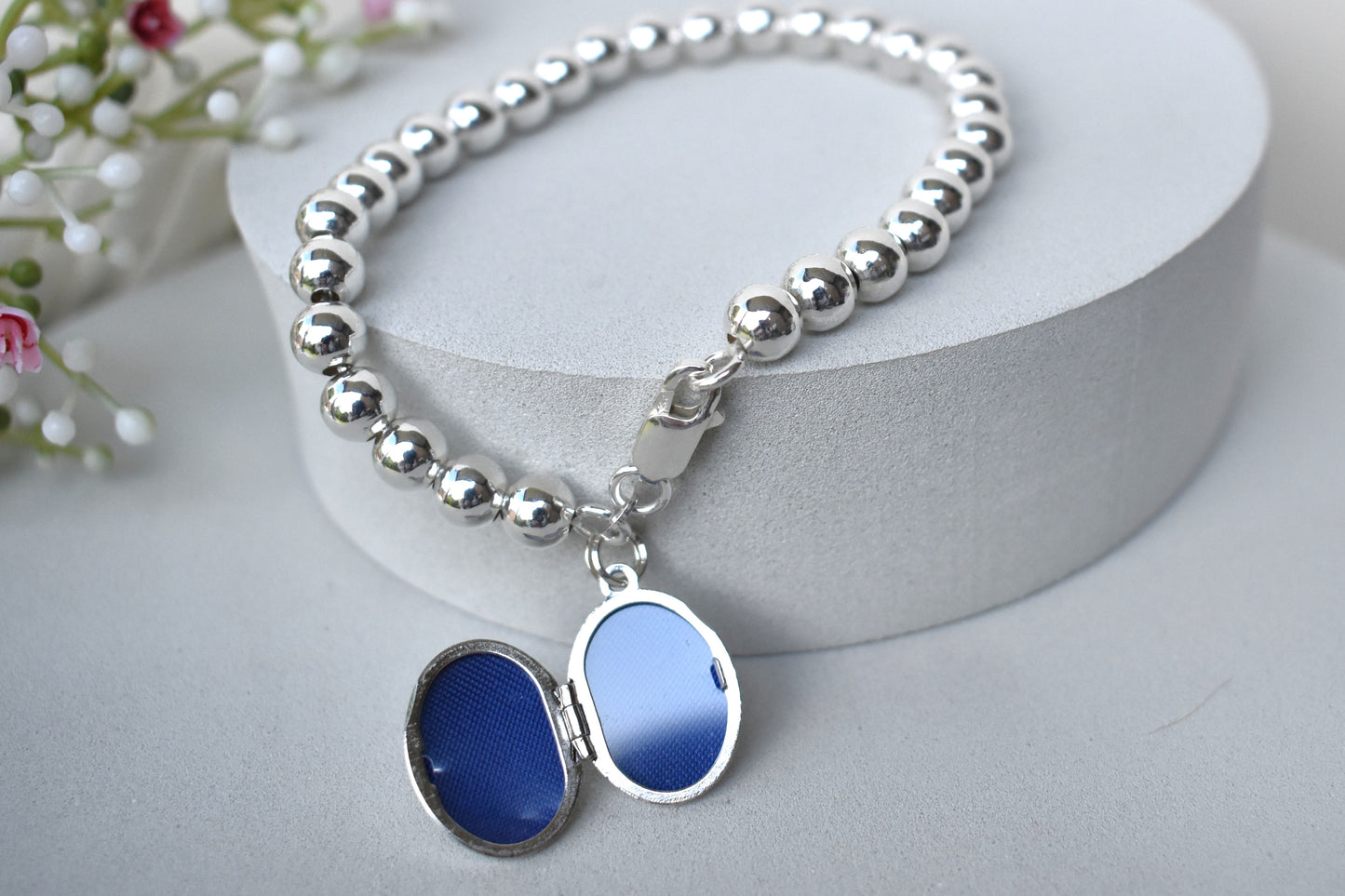 Sterling silver beaded bracelet with a lobster clasp. Next to the clasp is an oval locket that can be engraved with the wording of your choice