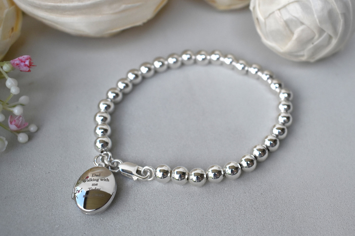 Sterling silver beaded bracelet with a lobster clasp. Next to the clasp is an oval locket that can be engraved with the wording of your choice