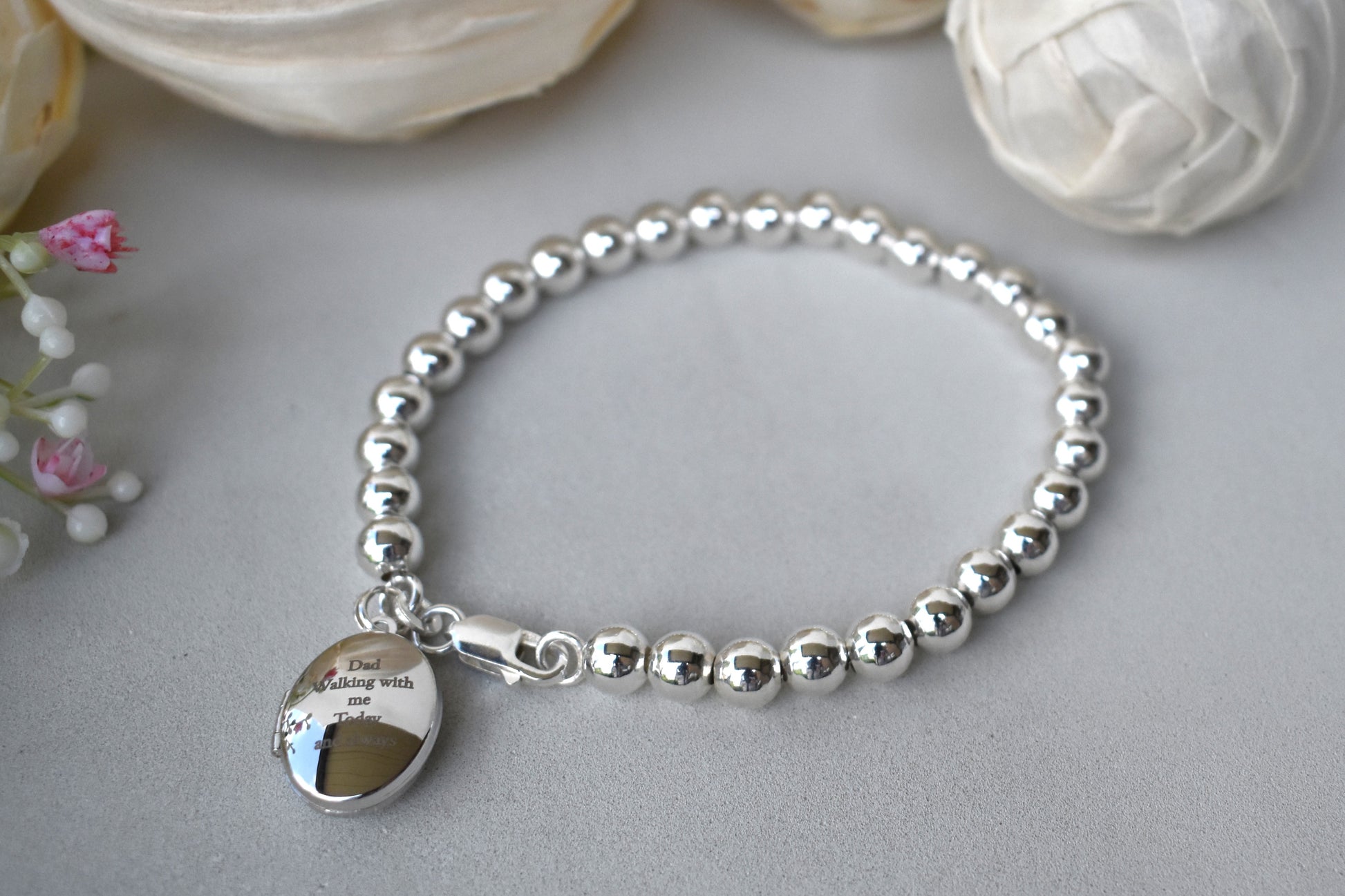Sterling silver beaded bracelet with a lobster clasp. Next to the clasp is an oval locket that can be engraved with the wording of your choice