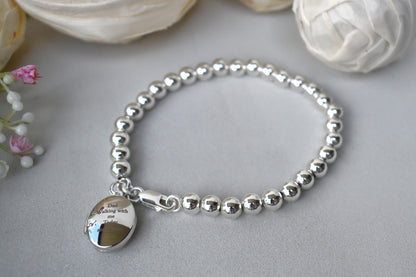 Sterling silver beaded bracelet with a lobster clasp. Next to the clasp is an oval locket that can be engraved with the wording of your choice