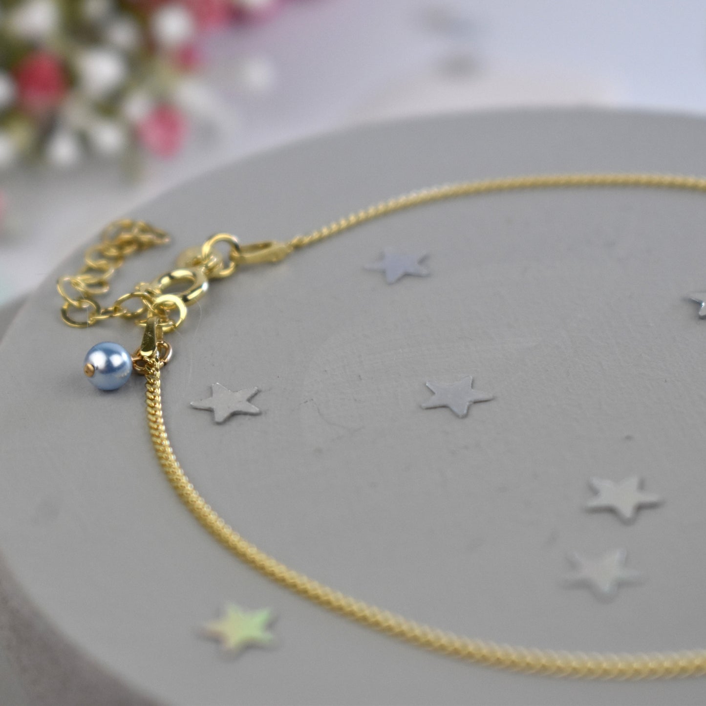 Close up of gold plated sterling silver curb anklet showing tiny blue glass pearl