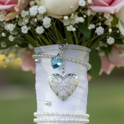 Wedding bouquet locket. A filigree locket that opens to take one photo is suspended from a sterling silver chain and next to a high quality pale blue crystal heart. The chain ends in a lobster clasp so that the charm can be fastened securely to th Bride's bouquet