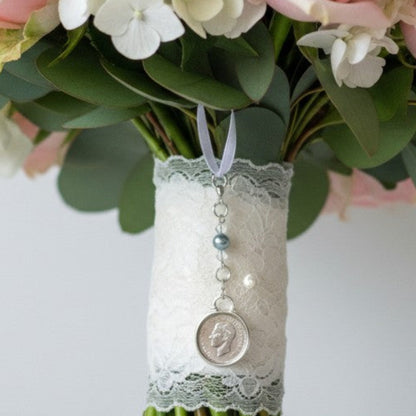 sixpence charm mounted on a chain with blue bead and crystals shown on bouquet