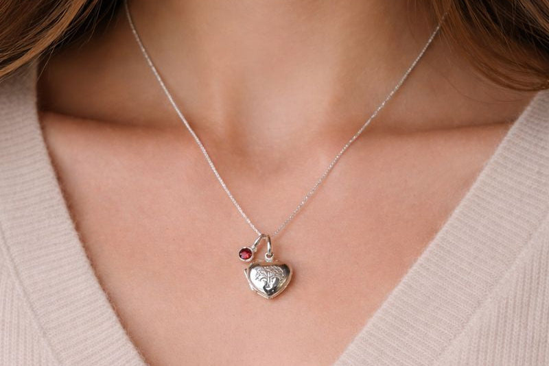 Sterling silver heart shaped locket with engraved family tree on the front. Opens to show space for two photos. Shown on an adjustable 16-18 inch sterling silver chain and with an optional birthstone. Shown worn