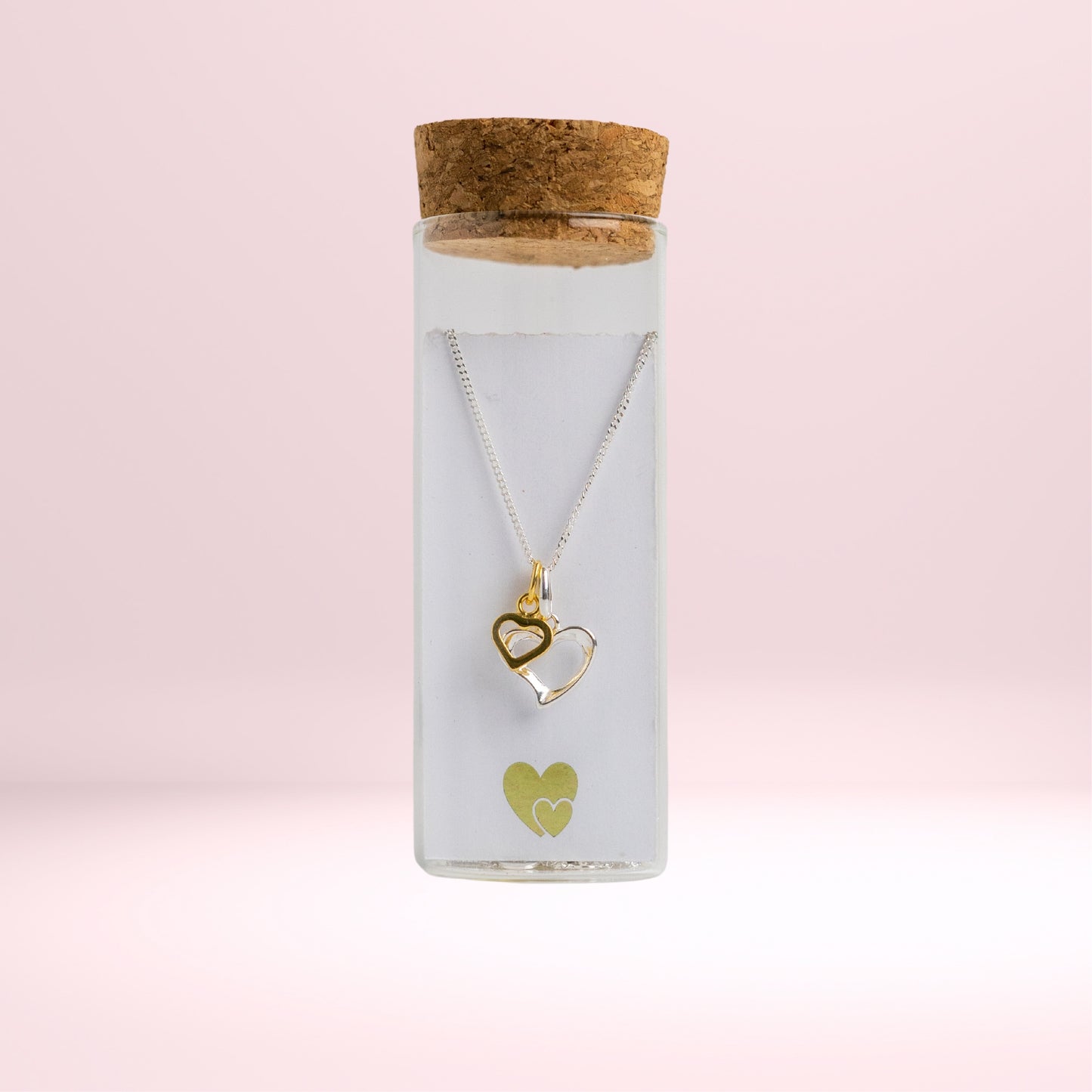 Message in a Bottle jewellery. A sterling silver heart is twinned with a smaller gold vermeil heart and suspended from a 16-18" sterling silver chain. The necklace is placed in a small glass bottle that includes a scroll personalised with a message of your choice.