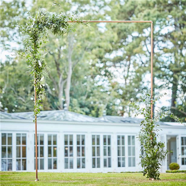 Square copper arch frame with standing feet. Shown with green foliage. Collapsable for easy storage