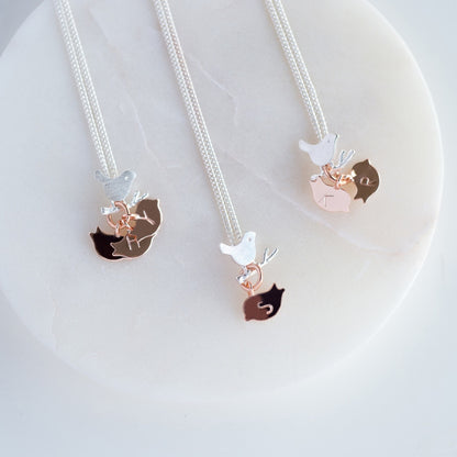 Various versions of a sterling silver necklace with a tiny silver bird on a branch. Below her are rose gold plated chicks each with an initial representing her child or children.
