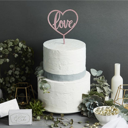 Rose gold finish acrylic cake topper. Heart shaped with the word "love" inside the heart, push into wedding cake