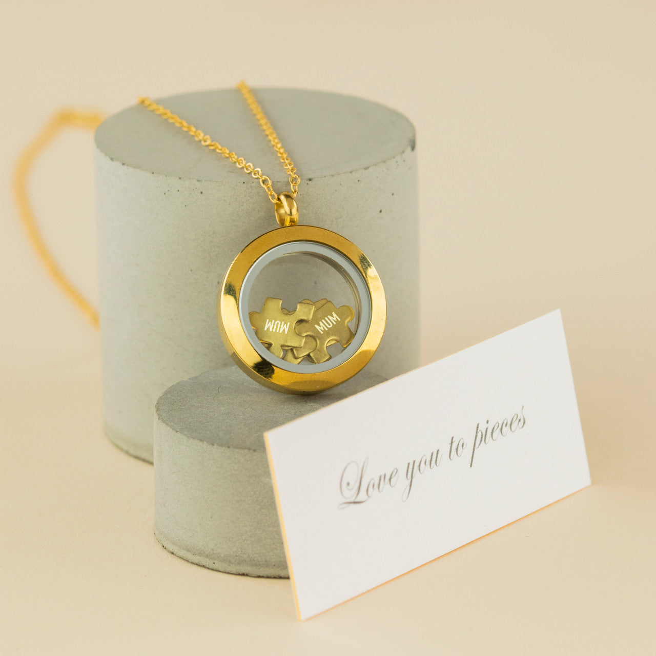 brass rimmed glass circle pendant with five brass jigsaw pieces inside. One piece says "Mum". The Love you to Pieces necklace.