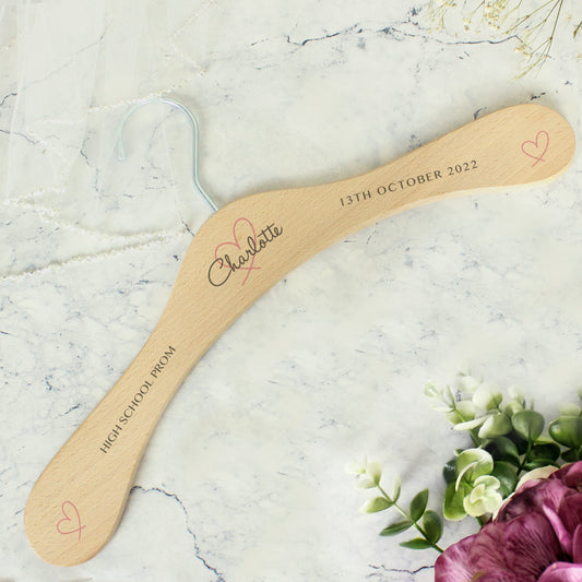 Personalised wooden wedding hanger in pretty heart design. Centre heart has  personalised name in script and there is room for two further lines of text on each arm of the hanger. Pretty pink heart adorns the centre of the hanger and the ends of the arms