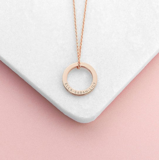 rose gold ring charm necklace, engraved with three names, each separated by a dash, suspended from a rose gold plated chain