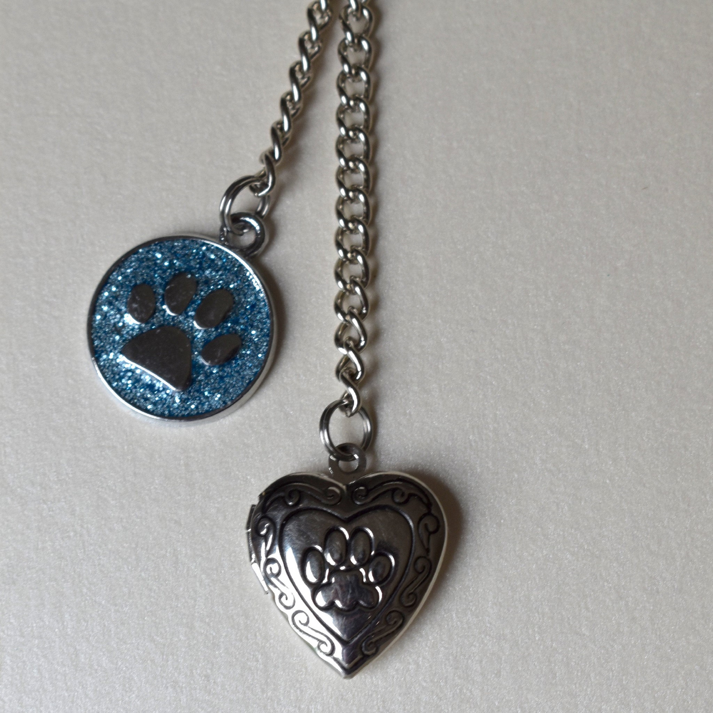 Heart shaped locket with paw print is teamed with a blue glitter charm, also with a paw print, part of  the pet memorial keyring