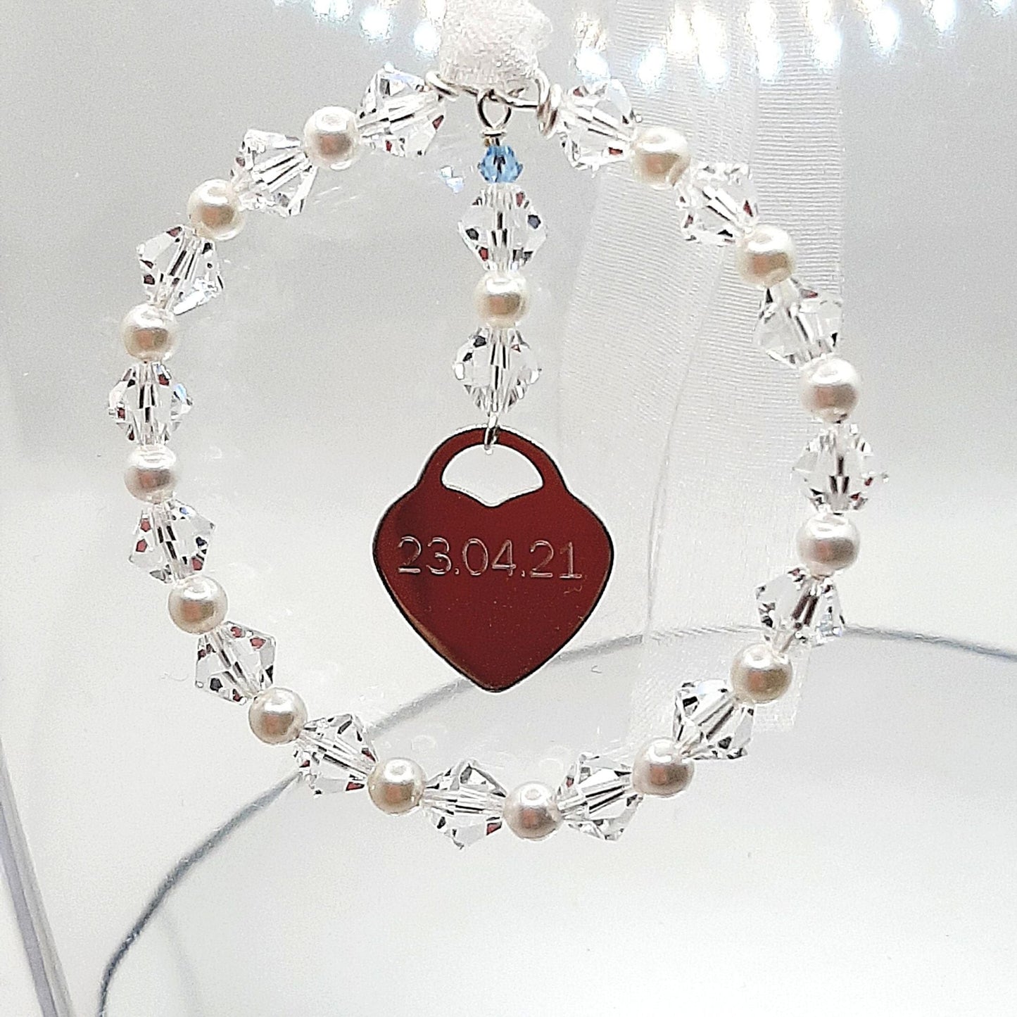 A wedding bouquet charm consisting of acircle of high quality crystals and glass pearls surround a sterling silver heart that can be engraved with names, dates or initials of your choice. Finished with white organza ribbon, the charm can be securely fastened to your wedding bouquet. The tiny blue bead is a nod to the "something blue" tradition