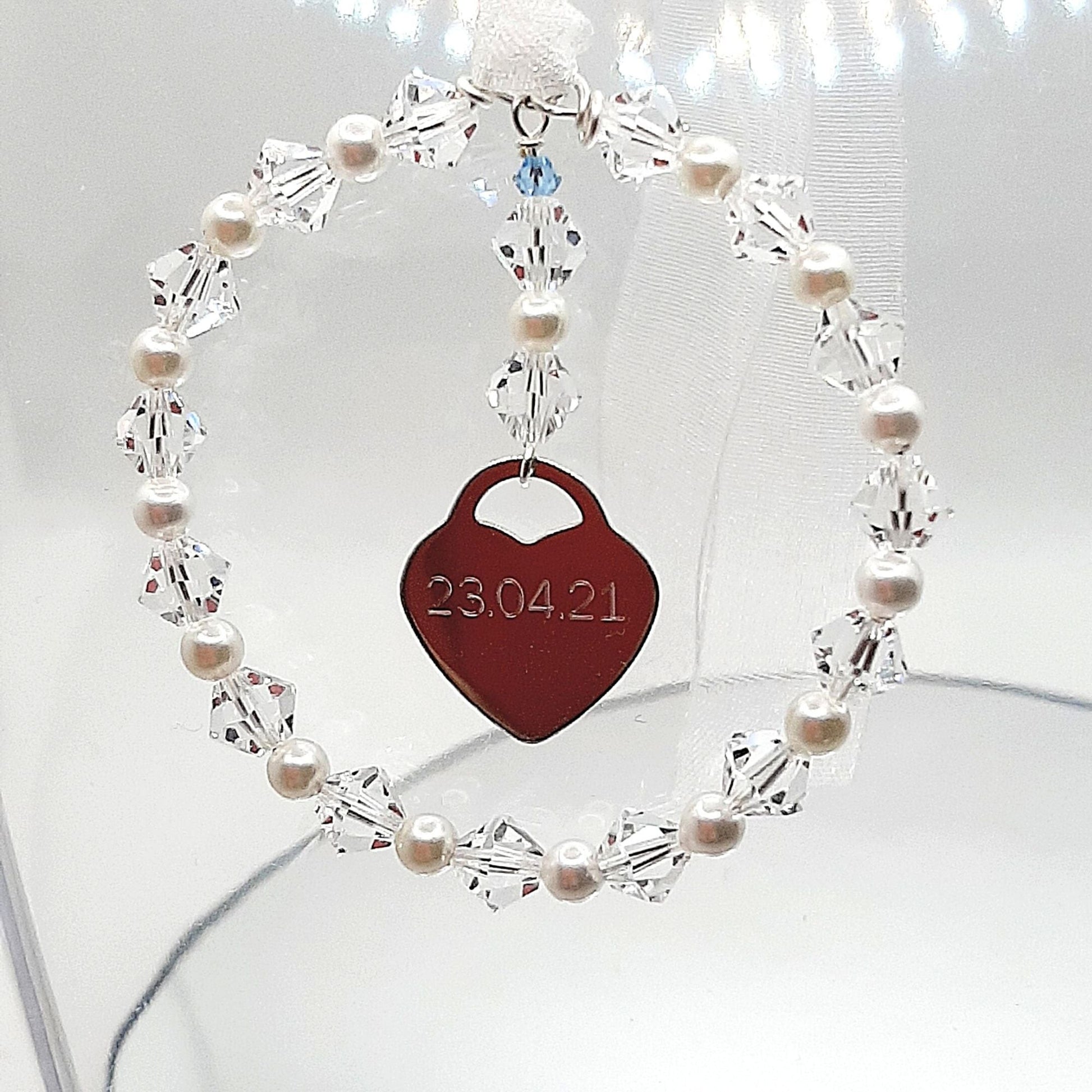 A wedding bouquet charm consisting of acircle of high quality crystals and glass pearls surround a sterling silver heart that can be engraved with names, dates or initials of your choice. Finished with white organza ribbon, the charm can be securely fastened to your wedding bouquet. The tiny blue bead is a nod to the "something blue" tradition
