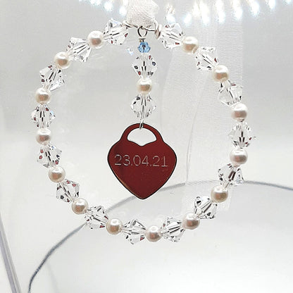 A wedding bouquet charm consisting of acircle of high quality crystals and glass pearls surround a sterling silver heart that can be engraved with names, dates or initials of your choice. Finished with white organza ribbon, the charm can be securely fastened to your wedding bouquet. The tiny blue bead is a nod to the "something blue" tradition