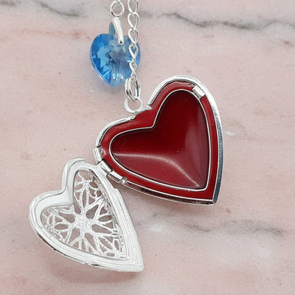 MWedding bouquet locket. A filigree locket that opens to take one photo is suspended from a sterling silver chain and next to a high quality pale blue crystal heart. The chain ends in a lobster clasp so that the charm can be fastened securely to th Bride's bouquetemorial locket open and with blue crystal heart. Shown open