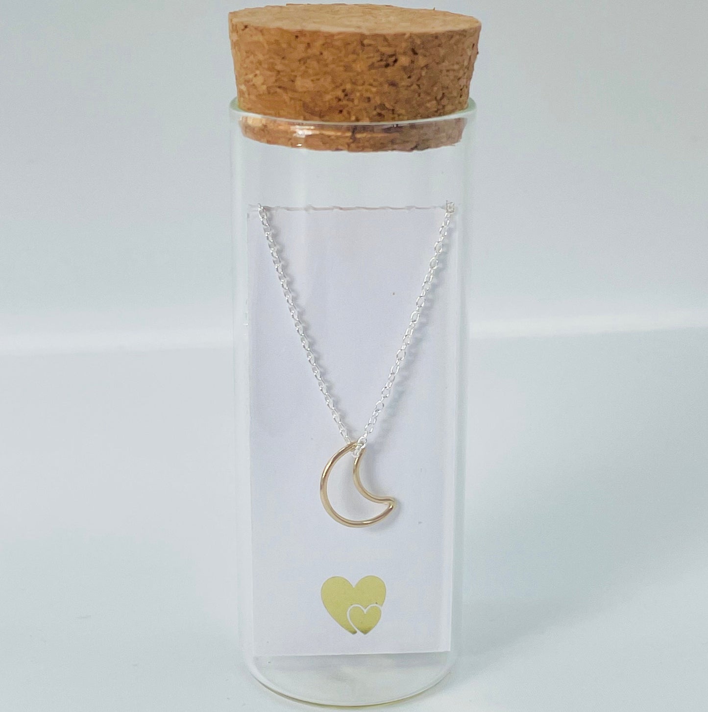 Gold vermeil hollow crescent moon hung from a sterling silver chain and placed in a glass bottle. Behind the card is a parchment scroll for you to add your own message.
