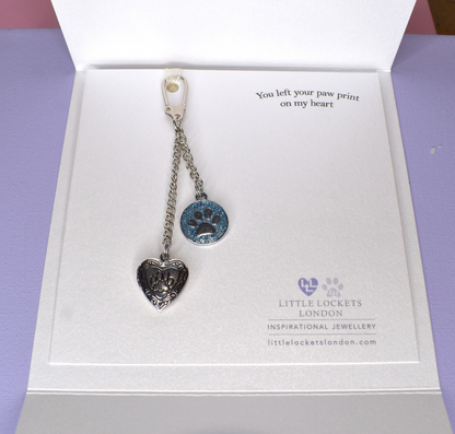 Heart shaped locket with paw print is teamed with a blue glitter charm, also with a paw print, shown with caribiner clasp and mounted on card with the message "You left a pawprint on my heart", placed in hand tied wallet