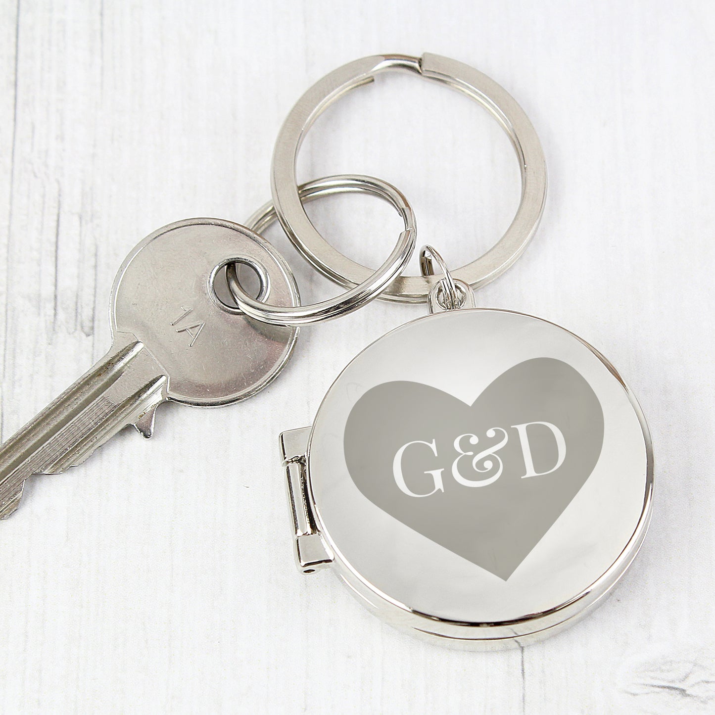 Round locket key ring. The heart motif on the front includes two initials of the couple. The locket opens to take two photos.