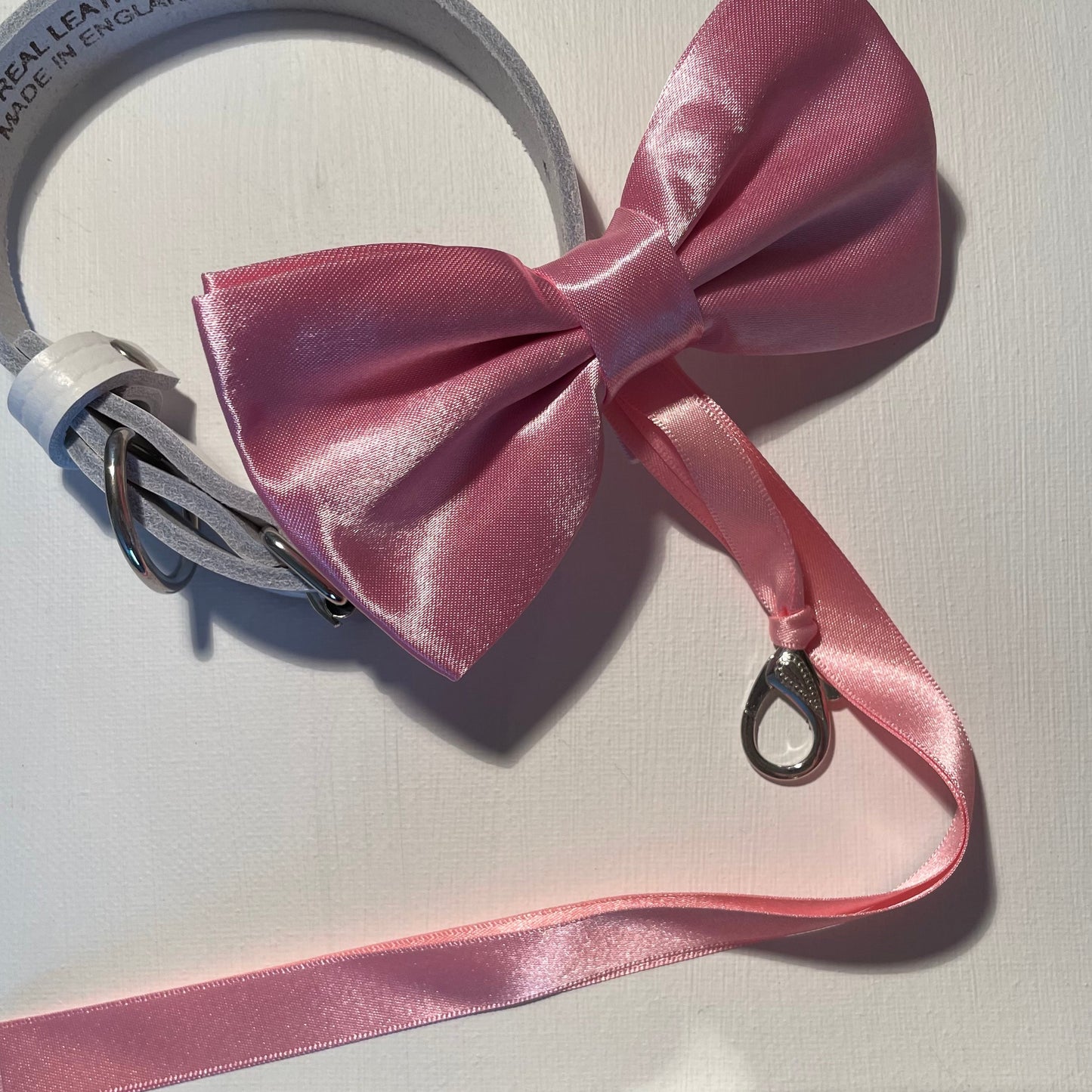 Pink satin bow tie shown with optional ring carrier and secured to a white leather collar